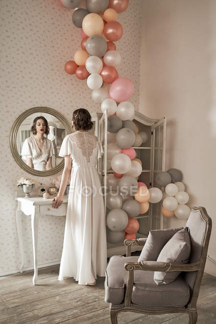 Привлекательная серьезная молодая женщина стоит и смотрит в большое круглое зеркало в будуаре — стоковое фото