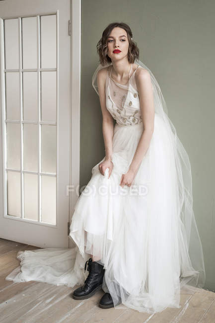 Mulher confiante adulto atraente em vestido branco e sapatos pretos militares inclinados na parede — Fotografia de Stock