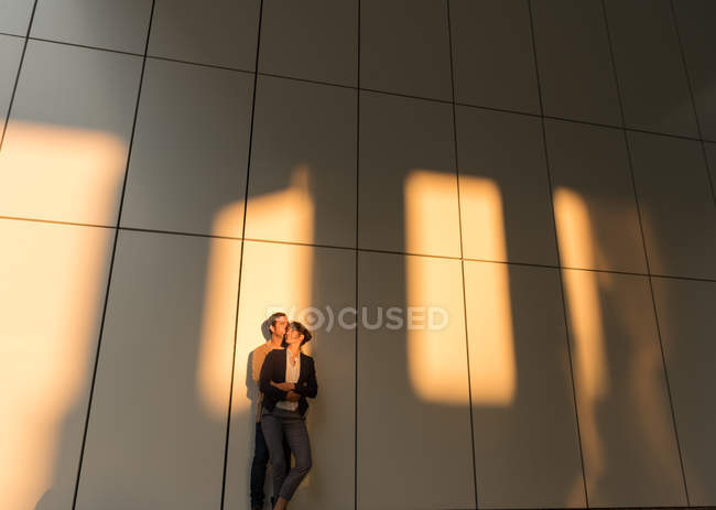 Businessman embracing and kissing girlfriend while standing outside modern building after work — Stock Photo