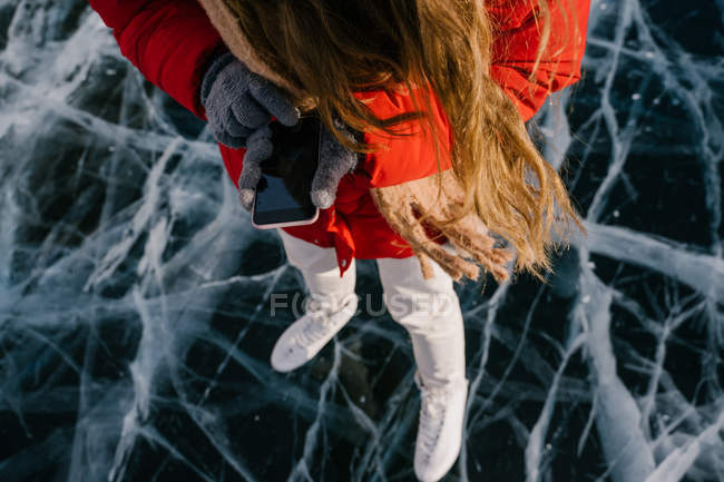 Обрезанное изображение женщины на коньках, стоящей на льду и использующей телефон — стоковое фото