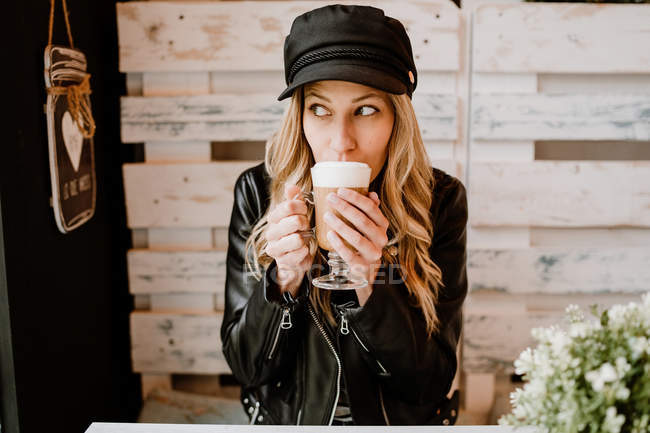 Mujer de pelo largo de moda beber delicioso café espumoso en la cafetería - foto de stock