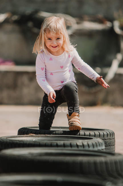 Feliz niña alegre que se divierte y caminar a través de la fila de neumáticos de coche negro mientras juega al aire libre en el día de verano - foto de stock