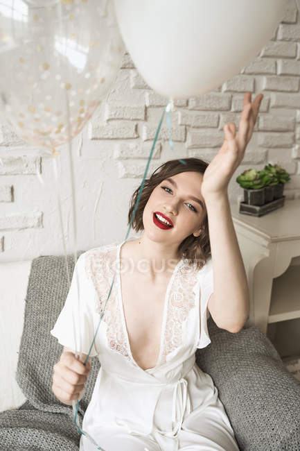 Hochwinkel der wunderschönen glücklichen Frau sitzt auf dem Sofa und hält Luftballons in heller Wohnung im Loft-Stil — Stockfoto