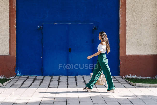 Молодая счастливая модная женщина, идущая по городу к голубой двери — стоковое фото