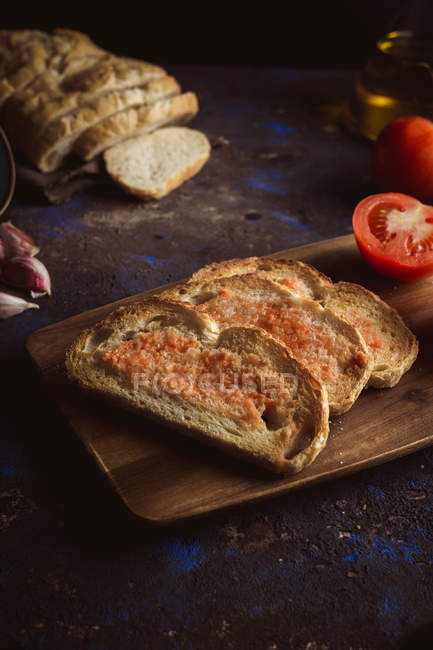 Spices, garlic and tomatoes near toasts on wooden board — Stock Photo