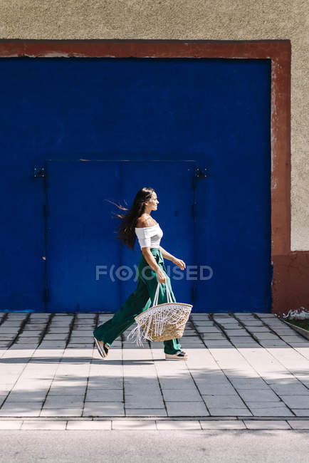 Молода щаслива модна жінка, що йде в місті на блакитні двері — стокове фото