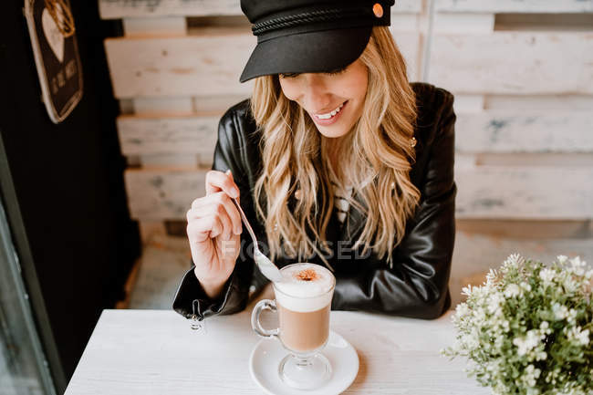 Long haired trendy beautiful blonde woman drinking from a glass of delicious foamy coffee — Stock Photo