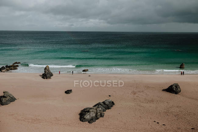 Пейзаж песчаного пляжа и бирюзового океана со скалами и людьми на заднем плане в Шотландии — стоковое фото