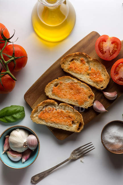 Especiarias, alho e tomates perto de torradas em tábua de madeira — Fotografia de Stock
