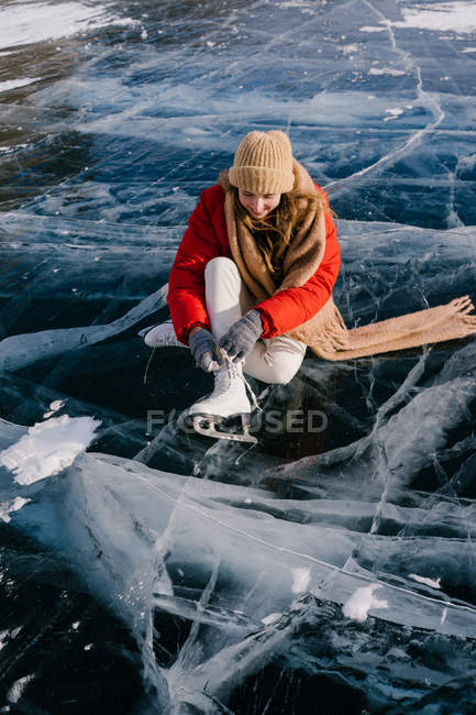 Mulher sentada no rio congelado e amarrando os atacadores — Fotografia de Stock