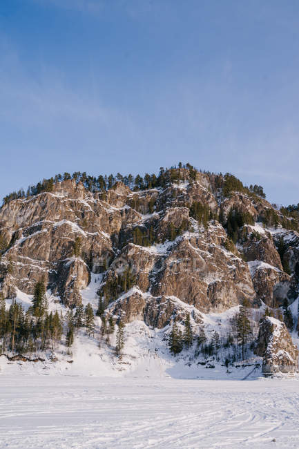 Paisaje escénico de valle nevado y majestuosas rocas cubiertas de nieve y abetos en el soleado día de invierno con cielo azul en Siberia Rusia - foto de stock