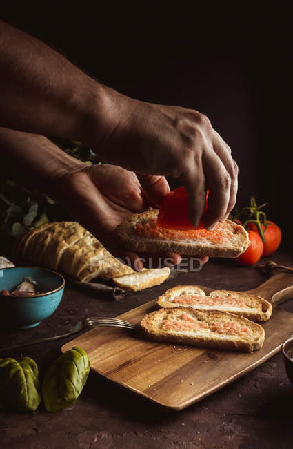 Mains de la personne versant des tomates sur des toasts — Photo de stock