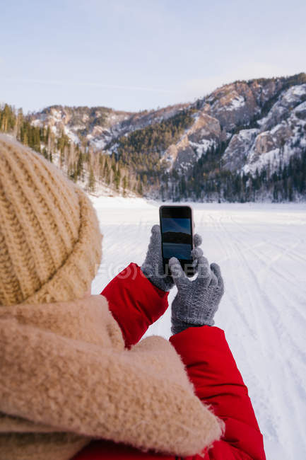 Image recadrée de femme en vêtements chauds et gants tricotés prenant des photos de la nature avec smartphone — Photo de stock