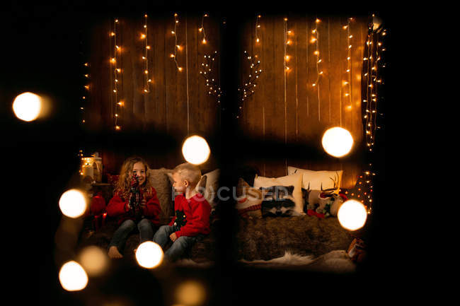 Blick durch das Fenster der Kinder spielen mit Spielzeug in gemütlichen Raum voller Weihnachtsdekoration — Stockfoto