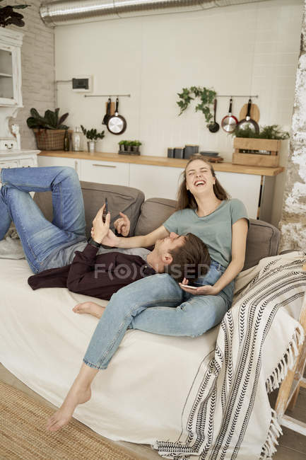 Calme réfléchi jeune homme et femme couché sur un canapé douillet confortable et surfer sur les téléphones mobiles à la maison — Photo de stock