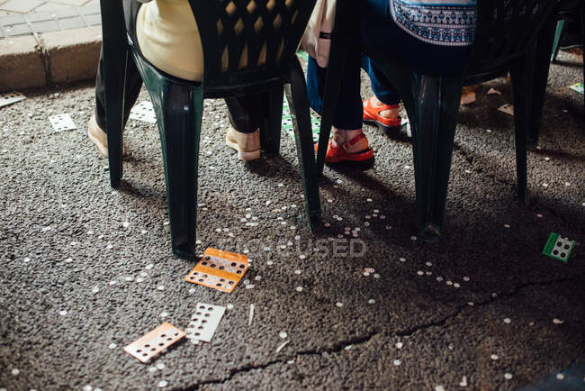 Зверху анонімні люди сидять на пластикових стільцях на асфальтній дорозі біля використаних лотерейних квитків під час ярмарку ввечері — стокове фото