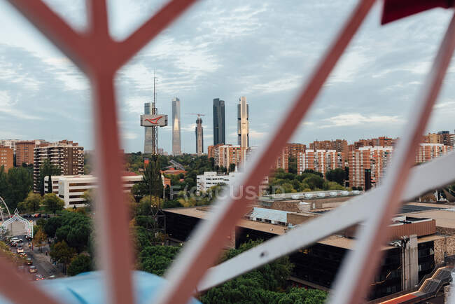 Arranha-céus e prédios de apartamentos atrás das grades da cabine da roda gigante no dia nublado na cidade — Fotografia de Stock