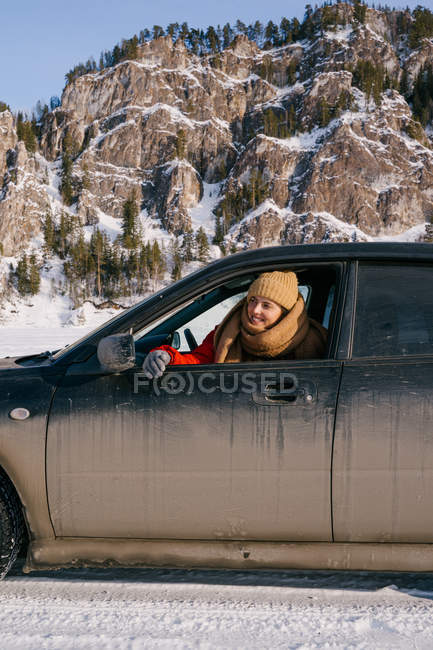 Woman leaning out car window on snowy valley — Stock Photo
