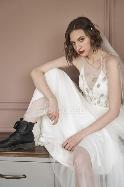 Привлекательная взрослая уверенная женщина в белом платье и черных военных туфлях, смотрящая в камеру — стоковое фото