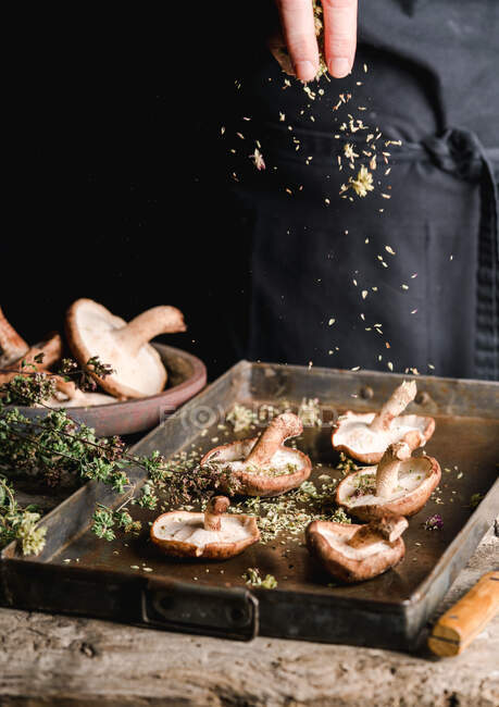 Erntehelfer streuen mit Kräutern frische braune Pilze Shiitake auf Metalltablett am rustikalen Holztisch — Stockfoto