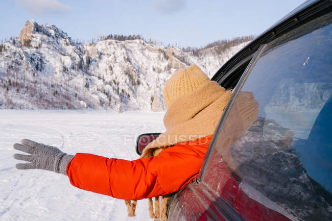 Vue arrière de la femme penchée par la fenêtre de la voiture sur la vallée enneigée — Photo de stock