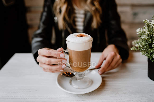 Cropped image of woman drinking from a glass of delicious foamy coffee — Stock Photo