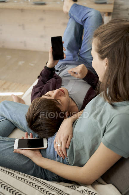 Calma riflessivo giovane uomo e donna sdraiato su accogliente divano morbido e navigare telefoni cellulari a casa — Foto stock