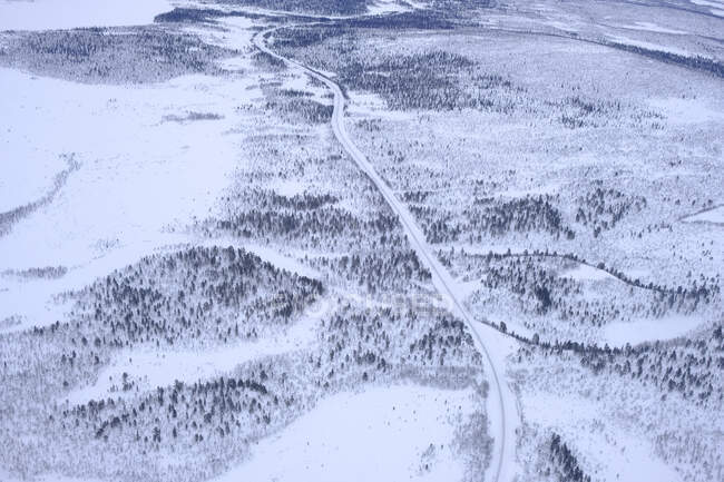 Drone view of narrow curvy road going through snowy fields and forests in nature — Stock Photo