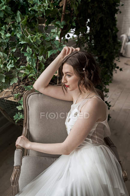 Gorgeous woman with red lips in white dress sitting on armchair — Stock Photo