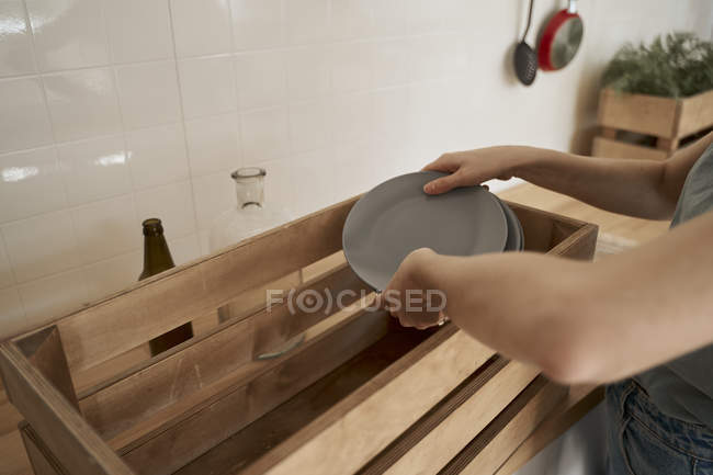 Hands of woman packing home dishware into wooden boxes at counter in kitchen — Stock Photo
