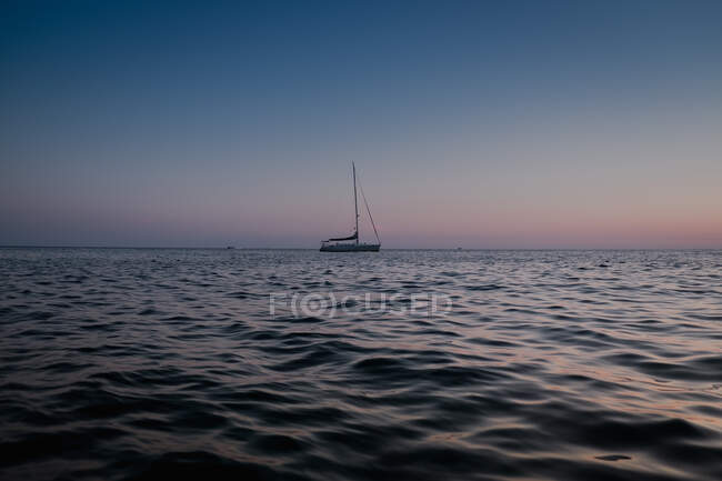 Seitenansicht des Segelbootes, das in der Abenddämmerung auf dem ruhigen Wasser des Meeres fließt — Stockfoto