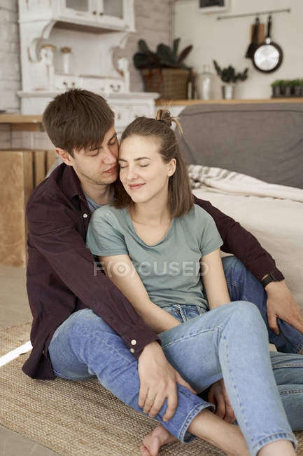 Calme couple charmant embrasser et profiter du repos assis pieds nus sur le sol dans le salon confortable — Photo de stock