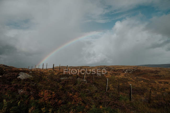 Landschaft des herbstlichen schottischen Feldes mit altem Zaun und regenbogendurchdringendem bewölkten Himmel — Stockfoto