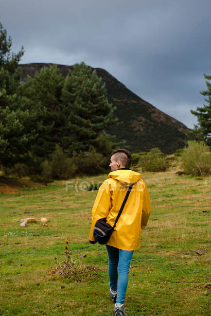 Погляд на жінку в жовтому плащі, що йде в лісі. — стокове фото