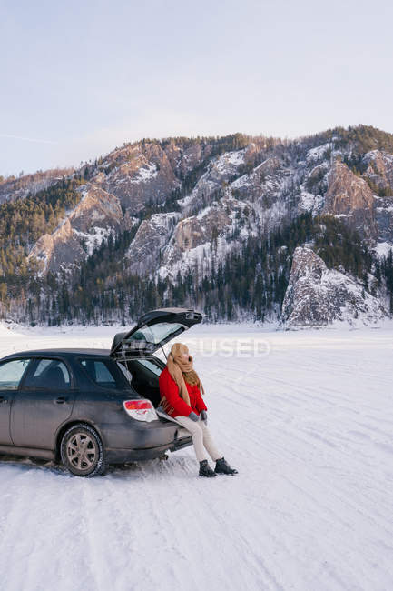 Woman sitting on car trunk in snowy valley — Stock Photo