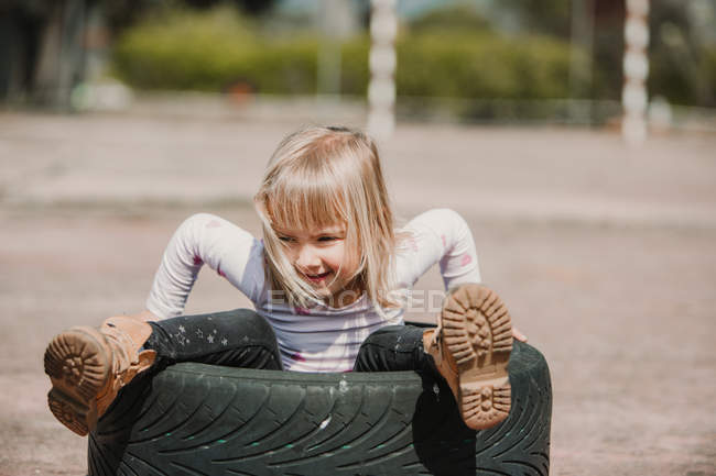 Von oben von glücklichen entzückenden kleinen Mädchen, die in Autoreifen sitzen, während sie Spaß haben und an Sommertagen draußen spielen — Stockfoto