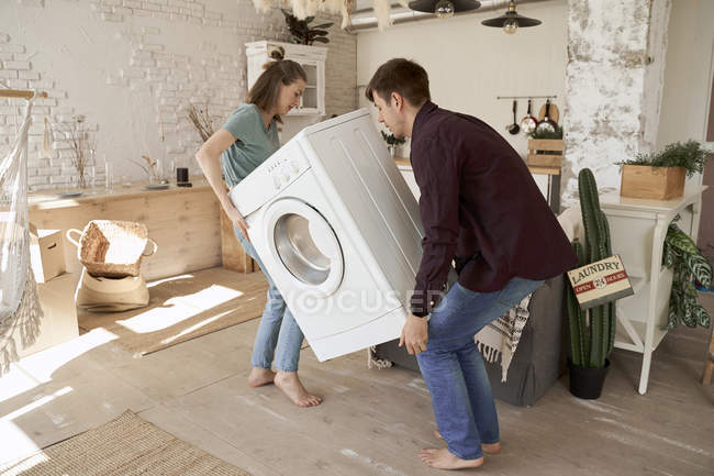 Side view of barefoot content man and woman carrying washing machine while moving to new house — Stock Photo