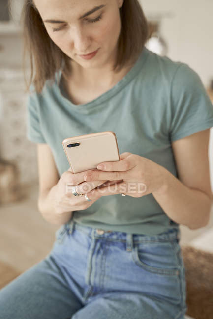 Chilling jovem mulher ter pausa e confortavelmente surfar telefone celular na cozinha espaçosa — Fotografia de Stock