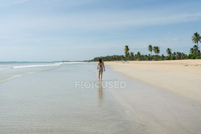 Giovane donna in acqua sulla spiaggia di sabbia con foresta tropicale — Foto stock