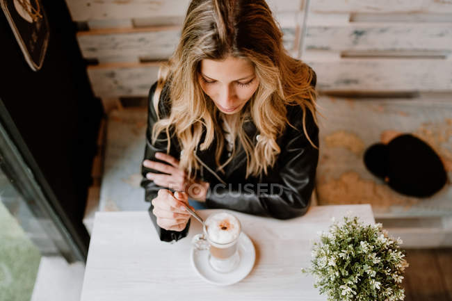 From above of long haired trendy beautiful blonde woman drinking from a glass of delicious foamy coffee — Stock Photo