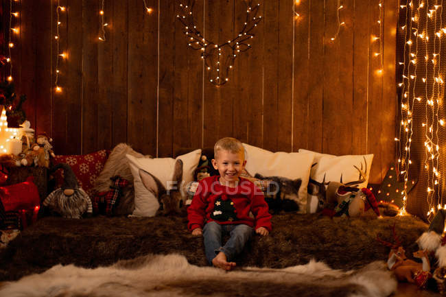 Очаровательный маленький мальчик сидит в комнате, полной рождественских украшений и смотрит в камеру — стоковое фото