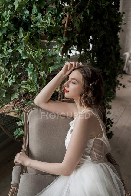 Preciosa mujer con labios rojos en vestido blanco sentada en sillón - foto de stock