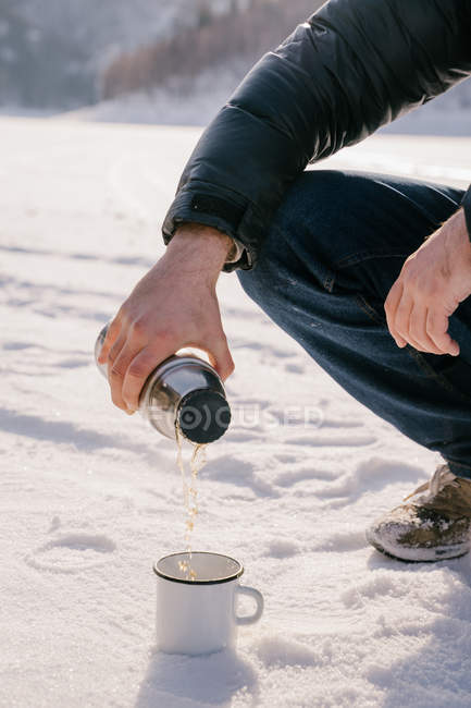Imagem cortada do homem derramando chá de garrafa térmica no dia de inverno — Fotografia de Stock