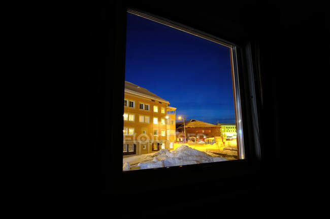 Case illuminate situate sulla strada della città dietro la finestra della camera oscura durante la notte invernale — Foto stock