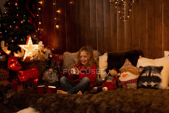 Приваблива дівчинка бавиться іграшками, сидячи в кімнаті, повній різдвяних прикрас. — стокове фото