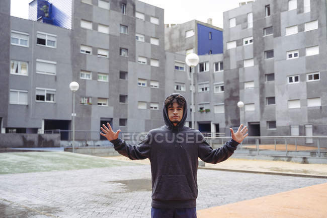 Man in hoodie standing looking at camera in between city buildings on background at cold day — Stock Photo