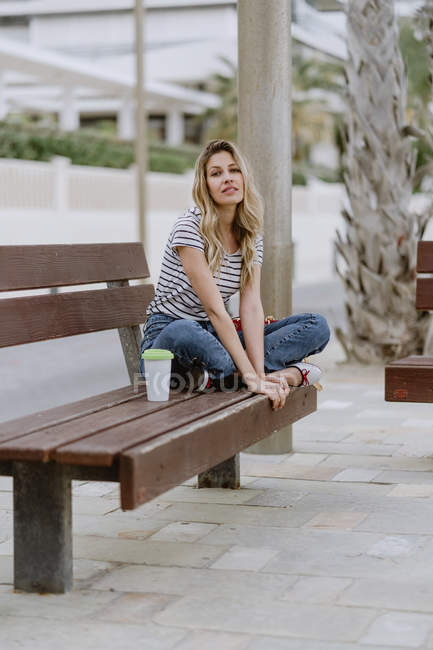 Впевнена випадкова жінка сидить на міській лавці на набережній в літній день, дивлячись на камеру — стокове фото