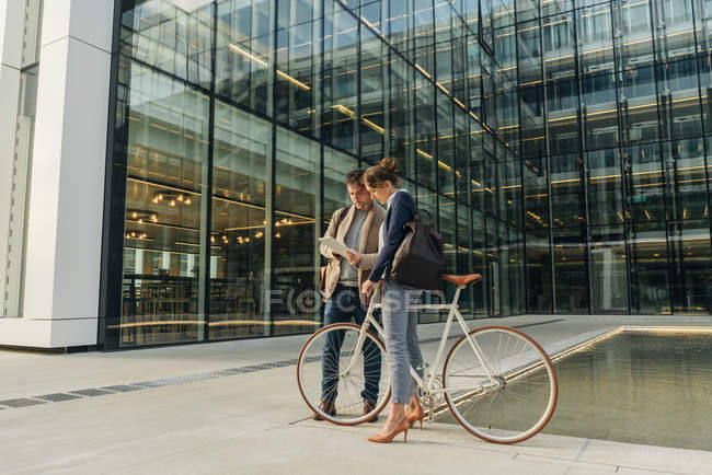Homme et femme joyeux avec vélo souriant et regardant une tablette tout en communiquant à l'extérieur de l'immeuble de bureaux sur la rue de la ville moderne — Photo de stock