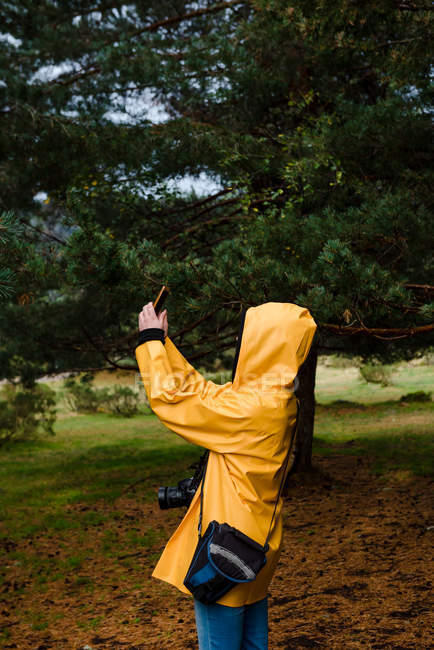 Vista lateral da mulher com capuz e capa de chuva amarela tomando selfie — Fotografia de Stock