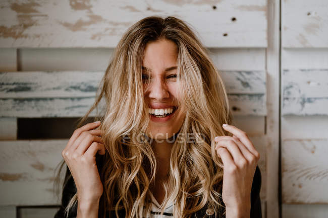 Stylish beautiful blonde woman in black jacket covering ears, squeezing head by hands and biting lips — Stock Photo